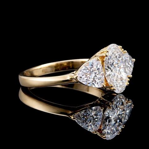 Gold engagement ring with large oval diamond and triangular accent stones on black reflective background