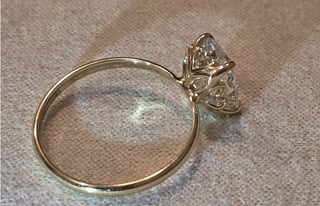 Gold solitaire engagement ring with diamond on beige textured surface