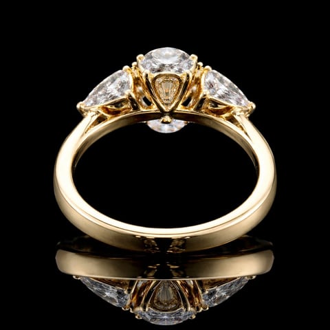 Gold three-stone diamond engagement ring with round center stone and trillion side stones on black background