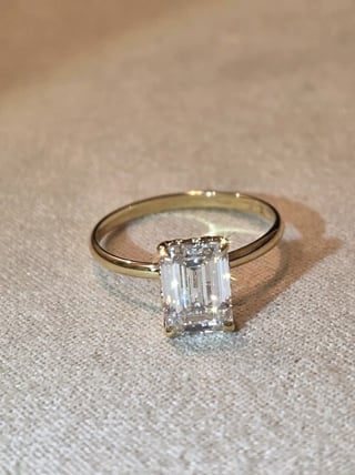 Gold engagement ring with rectangular cut diamond solitaire on beige textured surface