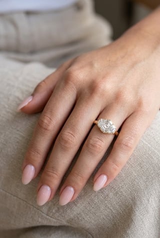 Close-up of a womans hand wearing a diamond engagement ring with pale pink manicured nails on a beige fabric background