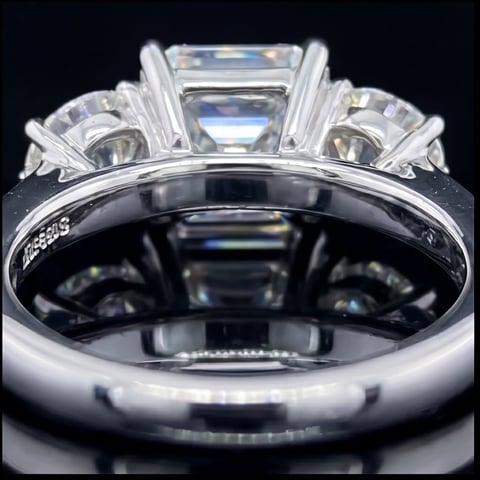 Back view of a luxury three-stone diamond ring with emerald-cut center stone and white metal band