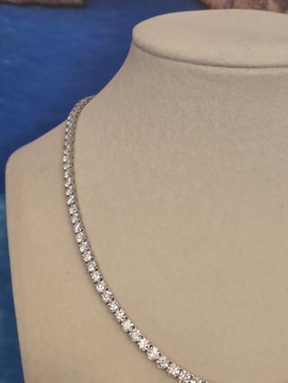 Diamond tennis necklace displayed on a beige mannequin bust against a blue background