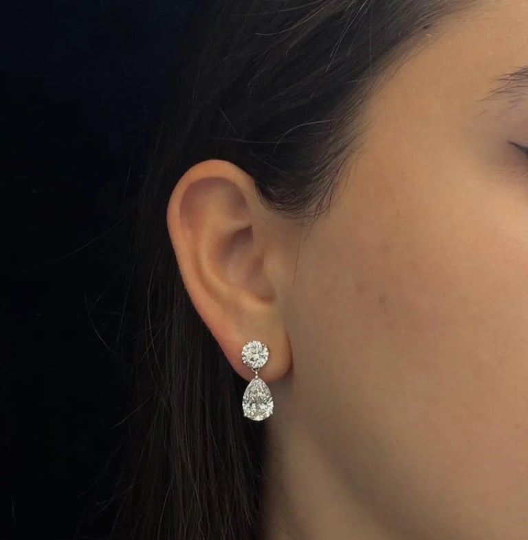 Woman wearing diamond drop earrings with round stud and teardrop shaped stone against dark background