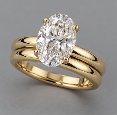 Gold engagement ring with oval-cut diamond solitaire stone on gray background
