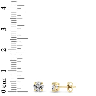 Pair of 14K yellow gold round diamond stud earrings, 1 ct total weight, beside a centimeter ruler