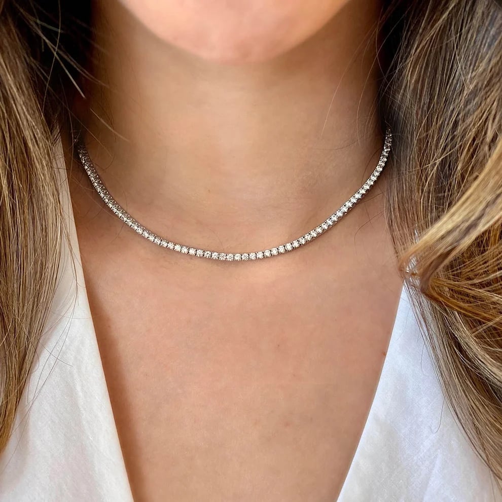 Woman wearing a sparkling diamond tennis necklace over white clothing