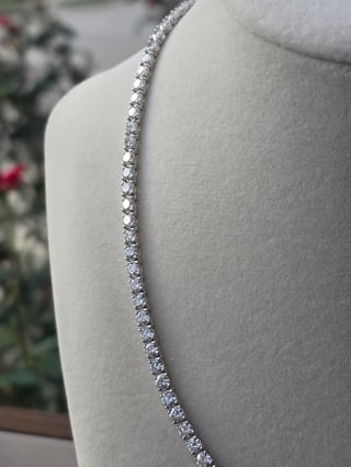 Elegant diamond tennis bracelet displayed on a cream-colored mannequin with blurred floral background
