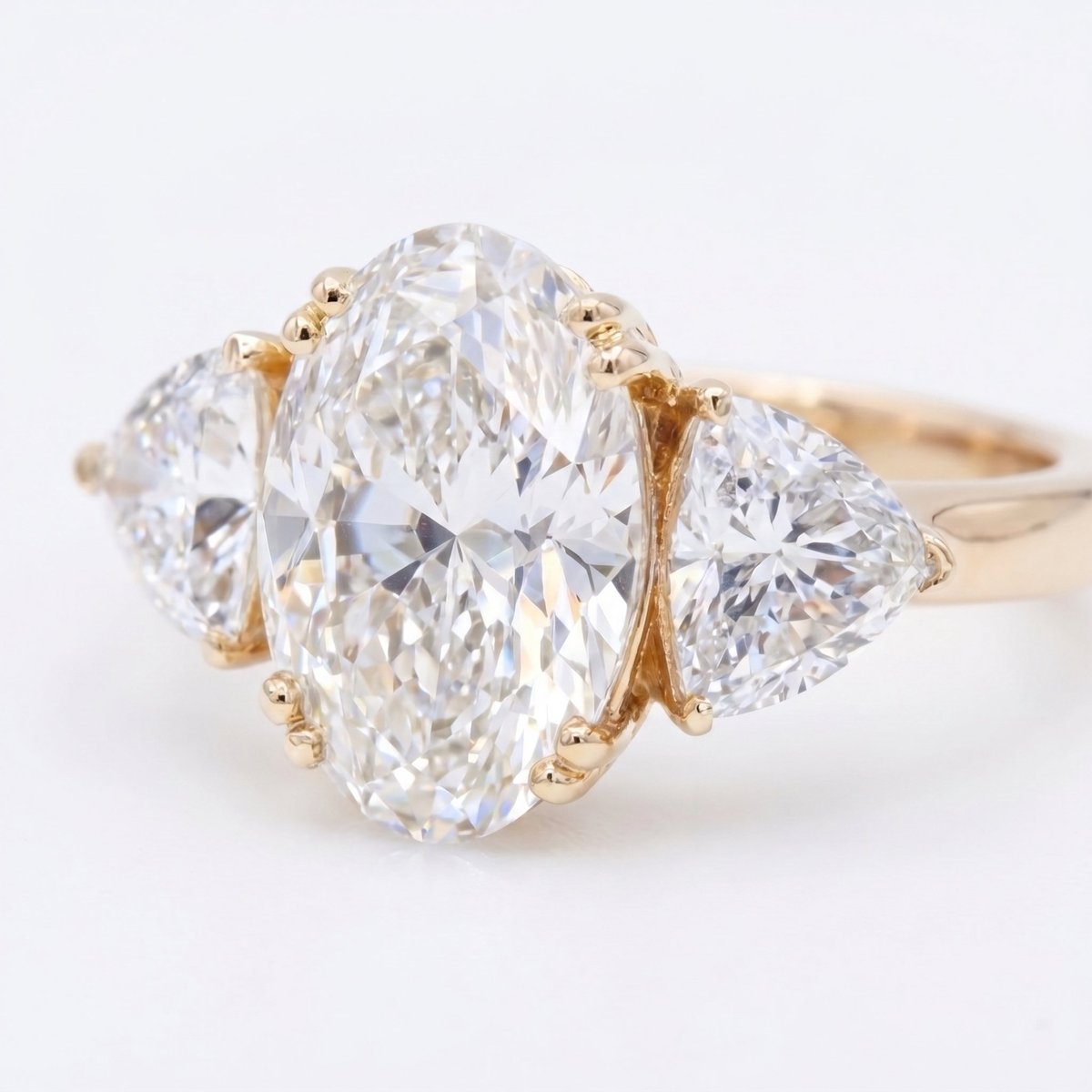 Three-stone diamond engagement ring with oval center stone and triangular side stones in gold setting