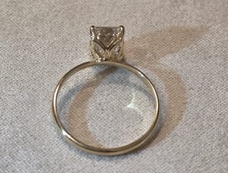 Gold solitaire engagement ring with square cut diamond on beige fabric background