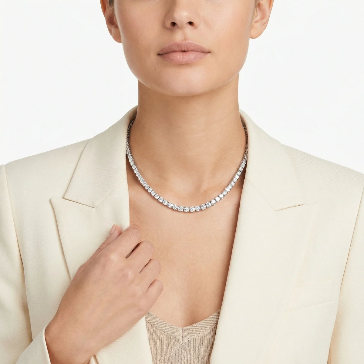 Person wearing a cream blazer and diamond tennis necklace, photographed from the shoulders up against a white background
